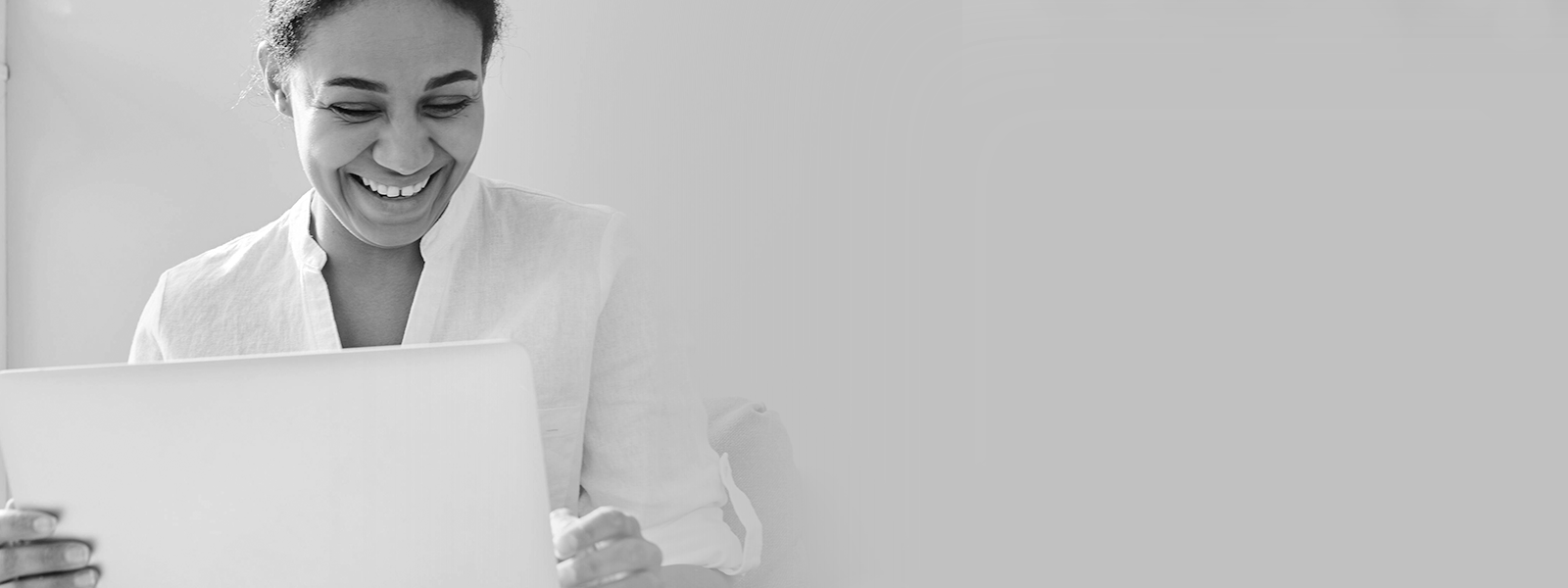 An woman african decent wearing a white shirt looking at a laptop screen and smiling.